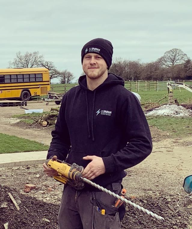 Stephen Sparham on site in branded S. Sparham Electrical workwear, holding an SDS drill
